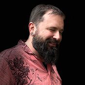 A man with a beard and mustache wearing a pink shirt.